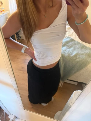 Vit oneshoulder topp i stretchigt tyg - Säljer en vit oneshoulder topp med tight passform. Toppen är croppad och har rynkade detaljer längs sidan för en snygg siluett. Tillverkad i ett stretchigt syntetmaterial som sitter bekvämt mot kroppen. Perfekt till sommarens outfits!