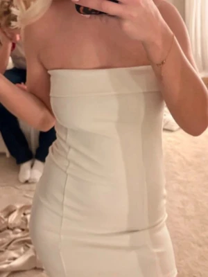 Vit axelbandslös kort klänning - Säljer en stilren vit axelbandslös kort klänning med figurnära passform. Klänningen har en enkel och elegant design utan synliga detaljer och passar perfekt till dig som gillar minimalistisk stil.