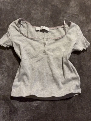 Ljusgrå kortärmad topp med knappar - Säljer en ljusgrå kortärmad topp med knappar, materialet är väldigt mjukt och skönt. passar jätte bra med jeans eller kjol 