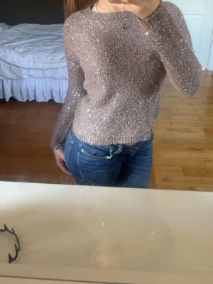 Glittrig beige stickad tröja - Supersnygg beige stickad tröja med glittriga inslag som ger ett festligt intryck. Tröjan har rund halsringning och långa ärmar. Perfekt att styla med jeans eller kjol för en trendig look.