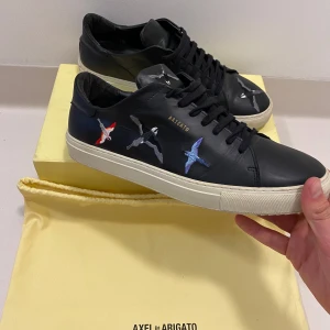 Svarta Arigato skor 45 - Svarta Axel Arigato sneakers med fåglar, (Storlek 45kr) mycket bra skick endast liten slitning som syns på sista bilden // Pris kan diskuteras || Skriv vid minsta fråga eller fundering💯🤝