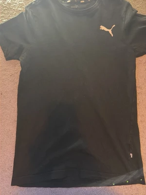 Svart t-shirt från Puma - Säljer en svart t-shirt från Puma med klassisk passform och korta ärmar. T-shirten har en vit Puma-logga på bröstet och är tillverkad i mjuk bomull som känns skön mot huden. Perfekt till en avslappnad stil.