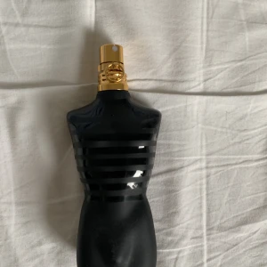 Jean Paul Gaultier Le Male Le Parfum - En ikonisk parfymflaska formad som en manlig torso i svart glas med matta och blanka ränder samt guldfärgad spraykork. Flaskan har en modern och edgy look som verkligen sticker ut på hyllan. Perfekt för dig som gillar unika designer och starka dofter.