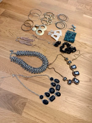 Stort smyckespaket med halsband & örhängen - Säljer ett mixat smyckespaket med flera halsband, armband och örhängen i olika färger och former. Innehåller chunky silverfärgat halsband, statementhalsband med svarta stenar, stora ringörhängen i guld och silver, geometriska örhängen, svarta armband och ett turkost pärlarmband. Perfekt för dig som gillar att variera din stil.