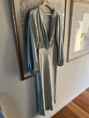 Ljusgrön långklänning - Snygg ljusgrön långklänning med v-ringning och långa puffärmar. Klänningen har snörning där fram där du kan dra åt och välja storlek själv i snörningen, och dragkedja i ryggen. Från Gina trolig storlek 40 men passar 38 och 42.