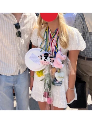 Vit kort klänning med puffärm - Superfin vit kort klänning med v-ringning och puffiga korta ärmar, perfekt till studenten. Klänningen har broderade blommor över hela tyget. Köpt på en dansk hemsida, minns tyvärr inte vad den hette. Använd en gång😊