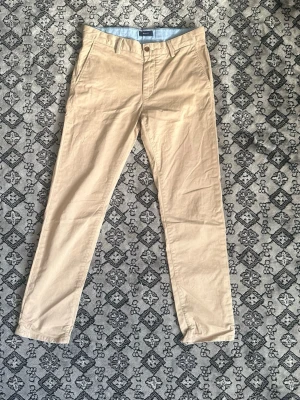 Beige chinos från Gant - Snygga beige chinos från Gant  med klassisk rak passform. Byxorna har framfickor, bälteshällor och två bakfickor med knapp. Tillverkade i mjukt bomullstyg som ger en clean och stilren look dessa chinos är perfekt nu till sommaren på en finare resturang eller bara en vardaglig uppklädnad. Dessa är i storlek 158/164 som borde passa mellan 12-14 år.