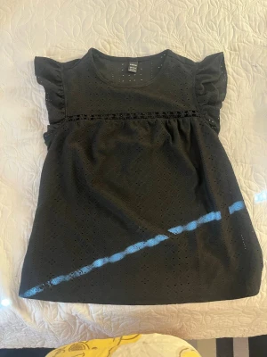 Svart tröja  - Snygg svart tröja med volangärmar och broderade håldetaljer.  har rund halsringning och en lös, rak passform. Perfekt för dig som gillar en enkel men ändå söt stil. Materialet känns lätt och luftigt.