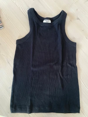 Svart ribbad linnetopp Kappahl - Snygg svart ribbad linnetopp från Kappahl. Modellen är ärmlös med rund halsringning och sitter tight mot kroppen. Perfekt att styla till jeans eller kjol för en enkel och clean look. Köparen står för frakt.