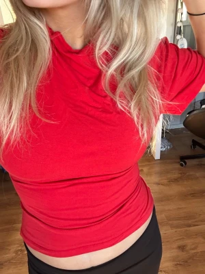 Röd croppad t-shirt med knyt - Snygg röd t-shirt med croppad passform och knyt i ryggen. T-shirten har korta ärmar och är tillverkad i ett mjukt material som känns skönt mot huden. Perfekt för dig som vill ha en enkel men trendig look.