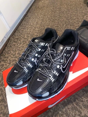 Nike svartvita sneakers - Snygga svartvita Nike sneakers med mesh och syntetdetaljer. Skorna har en sportig design med vita och silverfärgade detaljer, samt den klassiska Nike-loggan på sidan och tungan. Sulan är vit med svarta inslag och ger bra komfort. Perfekta för dig som gillar streetwear.