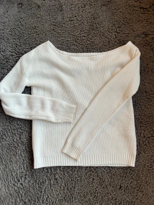 Vit ribbstickad tröja - Snygg vit stickad tröja med ribbstickat mönster och bred båtringning. Tröjan har långa ärmar och ribbade muddar vid ärmslut och nederkant. Perfekt att styla med jeans eller kjol för en clean look.