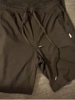Svarta shorts från Polo Ralph Lauren. - Svarta shorts från Polo Ralph Lauren med dragsko i midjan och klassisk logga broderad på ena benet. Sköna och stilrena, perfekta för sommaren. Tillverkade i mjukt bomullsmaterial och har en avslappnad proforma.