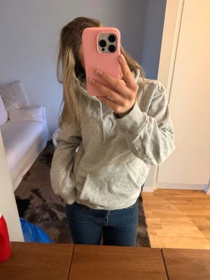 Ljusgrå hoodie med huva - Säljer en enkel och stilren ljusgrå hoodie med huva och känguruficka framtill. Hoodien har ribbade muddar vid ärmslut och nederkant.