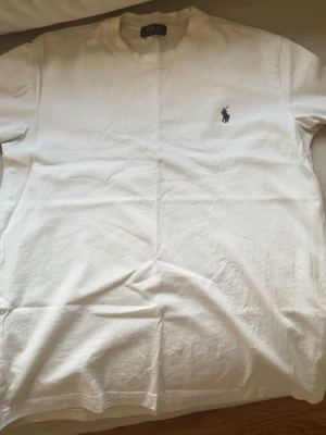 Vit t-shirt från Polo Ralph Lauren - Klassisk vit t-shirt från Polo Ralph Lauren med den ikoniska broderade loggan på bröstet. T-shirten har rund halsringning och korta ärmar. Tillverkad i mjuk bomull som känns skön mot huden. Perfekt basplagg till garderoben.
