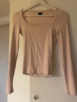 Ljusrosa långärmad topp - En enkel och stilren ljusrosa långärmad topp med rundad, bred urringning. Tillverkad i mjukt och stretchigt material som sitter skönt mot kroppen. Perfekt att matcha med jeans eller kjol för en clean look.