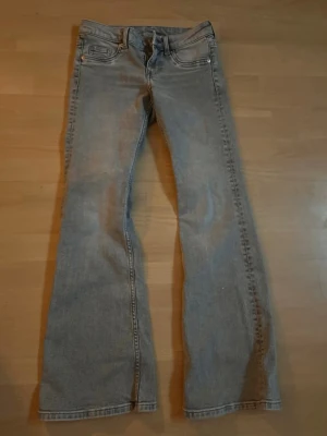 Ljusblå bootcut jeans - Säljer ett par ljusblå bootcut jeans med klassisk femficksdesign och normal midja. Jeansen har en lätt tvättad look och raka ben som går ut lite nedtill. Perfekta för dig som vill ha ett par bekväma jeans i denim.