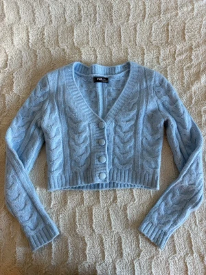 Ljusblå stickad knitwear - Ljusblå  kofta med v-ringning och fyra matchande knappar framtill. Kort modell med ribbade muddar och långa ärmar. Den är ifrån FBsister och är i storlek XXS, aldrig använd så i nyskick.