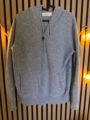 Grå cashmere hoodie från Sayless - Mjuk och stilren grå hoodie från Sayless i cashmere. Tröjan har dragkedja framtill, två fickor och huva med dragsko. Perfekt för en chill och avslappnad look. Säljer den pågrund av storlek köpt för ca 1000kr