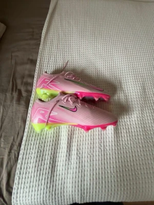 Nike fotbollskor  - Säljer ett par snygga Nike fotbollsskor i ljusrosa med neonrosa och limegröna detaljer. Skorna har klassisk snörning, låg profil och dobbar för spel på gräs. Swoosh-loggan syns tydligt på sidan och designen är riktigt modern och sportig. Storlek 44 10/10 skick aldrig använts. För fler bilder eller frågor skriv!