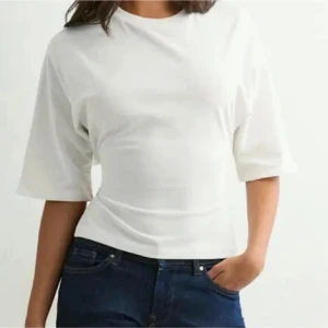 Open back tie tee från Nelly  - Säljer en trendig vit croppad topp med breda korta ärmar och snygg knytning i ryggen. Toppen har en stilren design med öppen rygg och är tillverkad i mjuk bomull. Perfekt för dig som vill ha en enkel men ändå unik look.