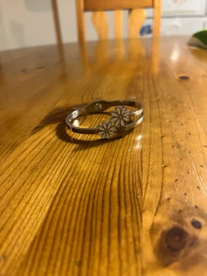 Silverfärgat armband med blommor - Snyggt armband i silverfärg med två vita blommor framtill. Blommorna har gult i mitten och armbandet har en öppen design som gör det lätt att ta på och av. Perfekt accessoar för dig som gillar en söt och stilren look💕
