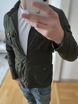Mörkgrön field jacket bommerang - Stilren mörkgrön field jacket med fyra framfickor och dragkedja framtill. Jackan har en klassisk krage och knappdetaljer på fickorna. Perfekt för dig som gillar en enkel men snygg look.