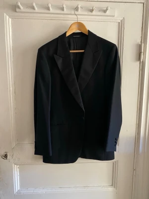 Svart kavaj från Oscar Jacobson - Stilren svart kavaj från Oscar Jacobson med klassiska slag och två knappar vid ärmslutet. Tillverkad i Sverige och helfodrad för en snygg siluett. Perfekt för dig som vill ha en tidlös och elegant look.