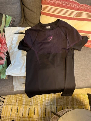 Gymshark Onyx v5💜 - Snygg svart träningströja från Gymshark med lila detaljer och logga på bröstet. Tillverkad i ett funktionsmaterial som andas, perfekt för gymmet eller löprundan. Kortärmad och med modern passform. ‼️ÄKTA, har köpt den från Gymshark som du ser på sista bilden. Helt ny, jätteskön och passar perfekt till gymmet. Hör av dig vid minsta funderingar eller frågor!