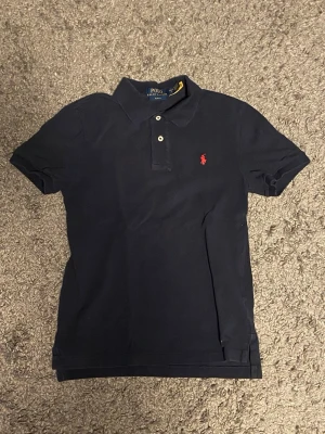 Marinblå Polo Ralph Lauren pikétröja. - Slim fit passform, L (14-16) inköpt från kids brand store under maj 2025. I fint använt skick.