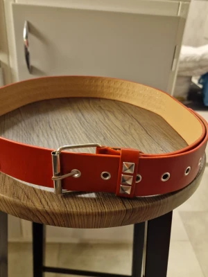 Skärp punk pyramidnitar röd - Punkbälte rött med pyramidnitar, designade i en Y2K metallpunkrockstil, utrustade med spänne i rostfritt stål. PU läder. Länd 100 cm. Bredd 3,6 cm. Dessa bälten är unisex, vilket gör dem perfekta för par, och de passar bra med jeans och vardagsbyxor.