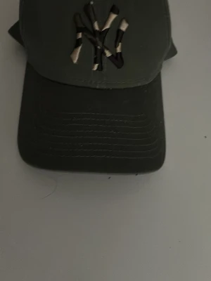 Grön New Era NY keps - Snygg grön keps från New Era med broderad NY-logga i camomönster på framsidan. Modellen är 9FORTY med böjd skärm och justerbar rem bak. Perfekt för dig som gillar streetwear och sportig stil. Kan diskutera pris