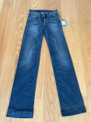 Blå raka jeans från 7 For All Mankind ginger - Snygga blå bootcut jeans från 7 For All Mankind med klassisk femficksdesign och subtila slitningar på låren. Jeansen har en rak passform med breda ben och är tillverkade i mjukt denim-material. Perfekt för dig som gillar en avslappnad och trendig look. Helt nya med lapp, w24 och långa i benen!