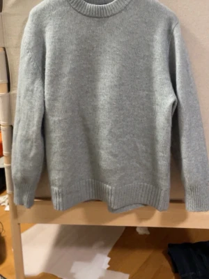 Gråblå fluffig stickad tröja med rund hals - En enkel och stilren ljusgrå stickad tröja med rund hals och ribbade muddar. Perfekt för att hålla sig varm under kyliga dagar. Tröjan har långärmad design och är gjord i mjukt stickat material som känns skönt mot huden. Tröjan e från hm o mysig som fon. Den e rätt fluffig i texturen 