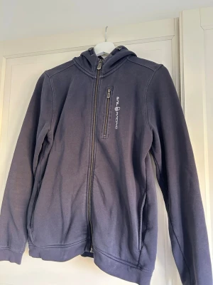 Mörkblå hoodie från Sail Racing - Säljer en mörkblå hoodie från Sail Racing med dragkedja framtill och en bröstficka med vit logga!!
