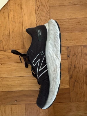 Svarta New Balance Fresh Foam sneakers - Snygga svarta sneakers från New Balance med Fresh Foam-sula. Skon har en stor vit logga på sidan och en tjock, vit sula med svarta detaljer undertill. Ovandelen är i mesh-liknande material för bra andningsförmåga och komfort. Perfekta för dig som gillar sportig stil.