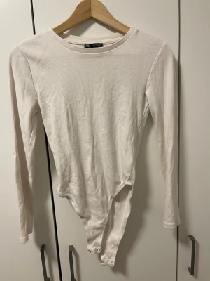 Vit ribbad body från Stradivarius - Säljer en enkel och stilren vit body från Stradivarius. Bodyn är ribbad, har långa ärmar och rund halsringning. Den stängs med tryckknappar i grenen och är gjord i ett mjukt stretchigt material som sitter snyggt på kroppen.