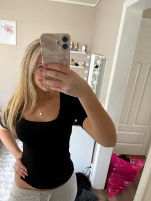 Svart tight topp med fyrkantig ringning - Snygg svart topp med tight passform och fyrkantig ringning. Toppen har korta ärmar och är tillverkad i ett mjukt, stretchigt material som sitter skönt mot kroppen. Perfekt att styla med både jeans och kjol.