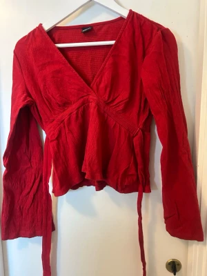 Röd knyt tröja från Gina tricot med långa ärmar❤️ - Trendig röd knyt tröja  med långa ärmar. Blusen har en djup V-ringning och är tillverkad i ett mjukt, lätt skrynklat tyg som ger en avslappnad men snygg look. I storlek small men passar även mindre eller större då man kan knyta tröjan så den passar som man vill. 