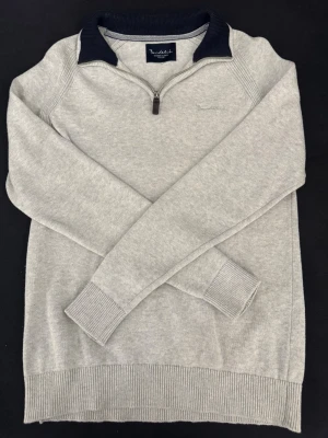 Ljusgrå tröja med dragkedja Bondelid - Ljusgrå långärmad tröja från Bondelid med halv dragkedja och mörkblå ribbad krage. Tröjan har ribbade muddar vid ärmslut och nederkant. Perfekt för lager-på-lager och snygg till jeans. Materialet känns mjukt och bekvämt.