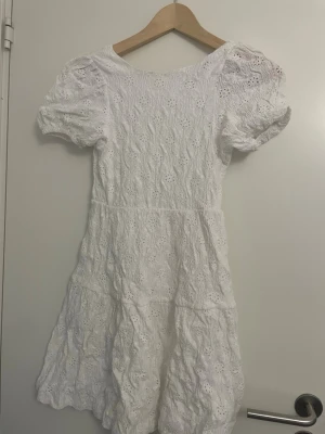 Vit spetsklänning med puffärm - Superfin vit klänning med broderad spets och puffärmar. Klänningen har kort längd och en öppen ryggdetalj. Perfekt för sommarens alla tillfällen och ger en romantisk vibe. Tillverkad i bomull för en luftig känsla.