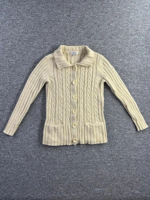 Tulchan kabelstickad cardigan S – Beige dam - Fin kabelstickad cardigan från Tulchan i storlek S (dam). Klassisk modell med krage, knäppning framtill och fickor. Tidlös beige färg som passar till allt 🤍  📏 Storlek: S 📐 Mått visas i bilderna ✨ Skick: Fint skick – skicket visas tydligt i bilderna  Perfekt till höst & vinter eller lager-på-lager.  💸 Följ mig så får du 10% rabatt på köpet!
