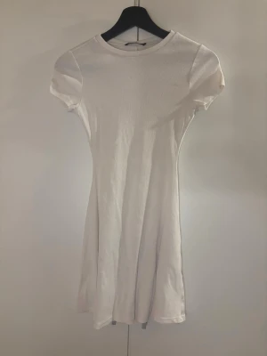 Vit kort ribbad klänning - En enkel och stilren vit kortklänning med ribbad struktur och rund hals. Klänningen har korta ärmar och en lätt utställd passform som ger en feminin siluett. Perfekt för varma dagar och enkel att styla med accessoarer. Den är lite genomskinlig💕