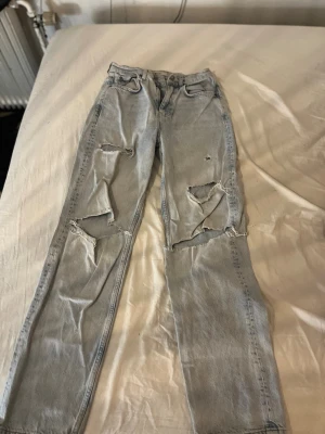 Ljusblå ripped jeans med raka ben - Säljer ett par ljusblå jeans med raka ben och stora slitningar framtill för en cool och avslappnad look. Jeansen har klassisk femficksdesign och är tillverkade i denim. Perfekta för dig som gillar streetstyle och vill sticka ut. Säljer dem då dem inte passar mig längre! Pris går att diskutera 