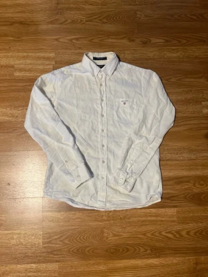 Vit skjorta från GANT i bomull - Klassisk vit skjorta från GANT i bomull med button-down krage och bröstficka med liten logga. Perfekt för en clean och stilren look. Casual fit och långa ärmar med knappar vid manschetterna. Också perfekt för den som vill klä sig mer åt grisch hållet 