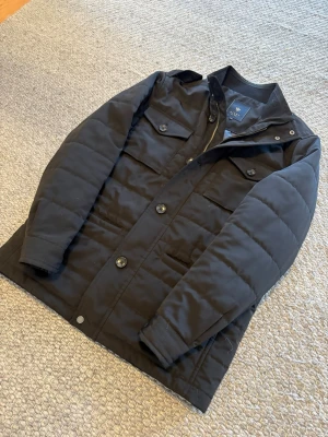 Fieldjacka från Riley  - Snygg svart fieldjacka från Riley i storlek 48 vilket motsvarar typ storlek S-M. Mycket bra skick nästan helt ny och inga tecken på användning.