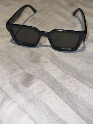 Svarta kantiga solglasögon - Snygga svarta solglasögon med kantig, modern form och bred båge. Glasen är mörka och ramen är i blank plast som ger en cool och trendig vibe. Perfekta för att lyfta vilken outfit som helst.