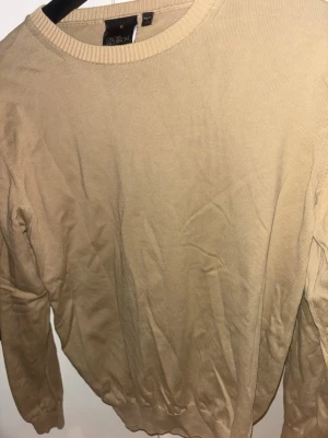 Beige tröja från Oscar Jacobson - Snygg beige tröja från Oscar Jacobson med rund halsringning och ribbade muddar. Tillverkad i Italien och har en klassisk, stilren design som passar perfekt till jeans eller chinos. Nytt skick vid snabb strykning använd få gånger.