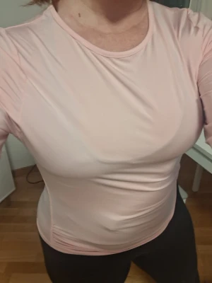 Ljusrosa långärmad topp - En enkel och stilren ljusrosa långärmad topp med rund halsringning. Toppen har en tight passform och är tillverkad i ett mjukt, stretchigt material som känns skönt mot huden. Perfekt att matcha med jeans eller kjol för en clean look. Aldrig använd men lapparna är bortklippta. 