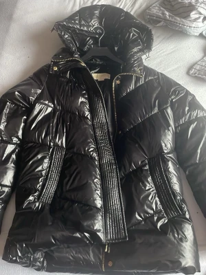 Michael Kors jacka - Den e xxs men ja brukar ha S-L och den passar mej.Snygg svart pufferjacka från Michael Kors med glansig finish, dragkedja i guld och huva. Jackan har quiltade detaljer och breda ribbade partier vid dragkedjan och fickorna. Perfekt för kalla vinterdagar och ger en trendig look.